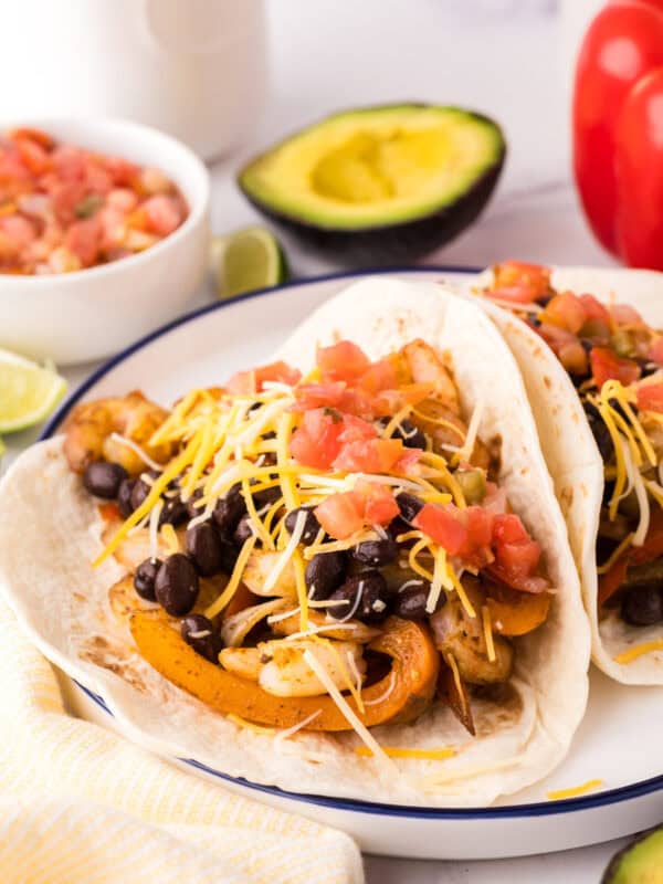 shrimp fajitas served over flour tortillas on a plate with fresh veggies all around.