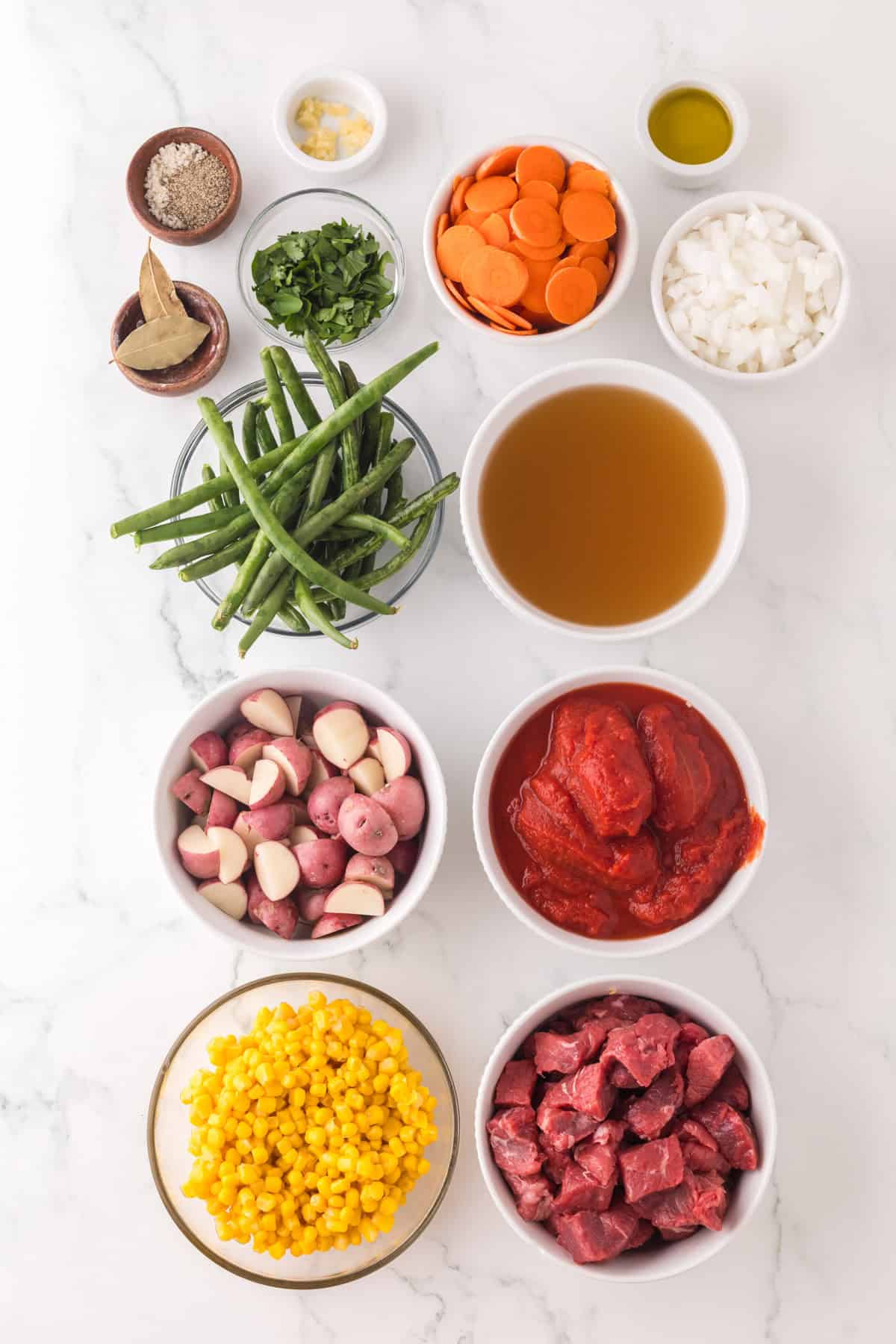 portion bowls each with raw ingredients to make slow cooker beef veggie soup.