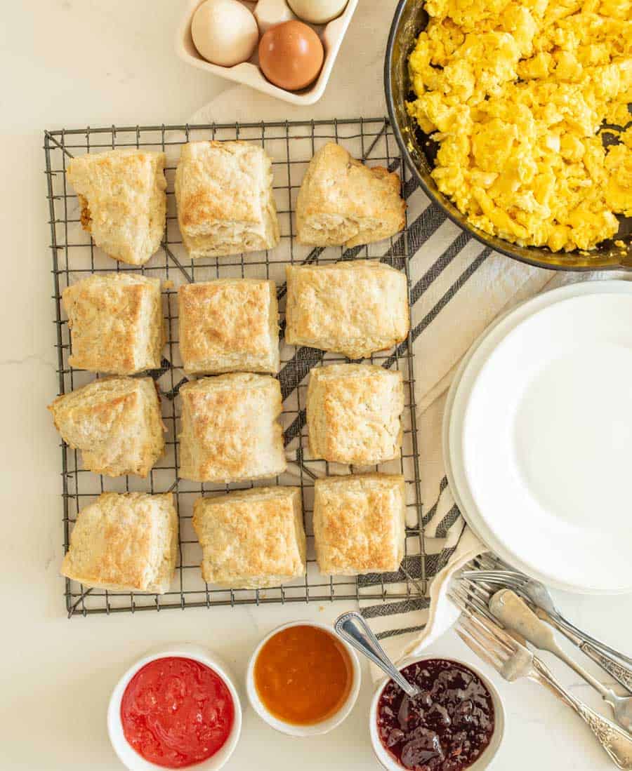 sourdough biscuits on a cooling rack in a breakfast photo with scrambled eggs and jam.