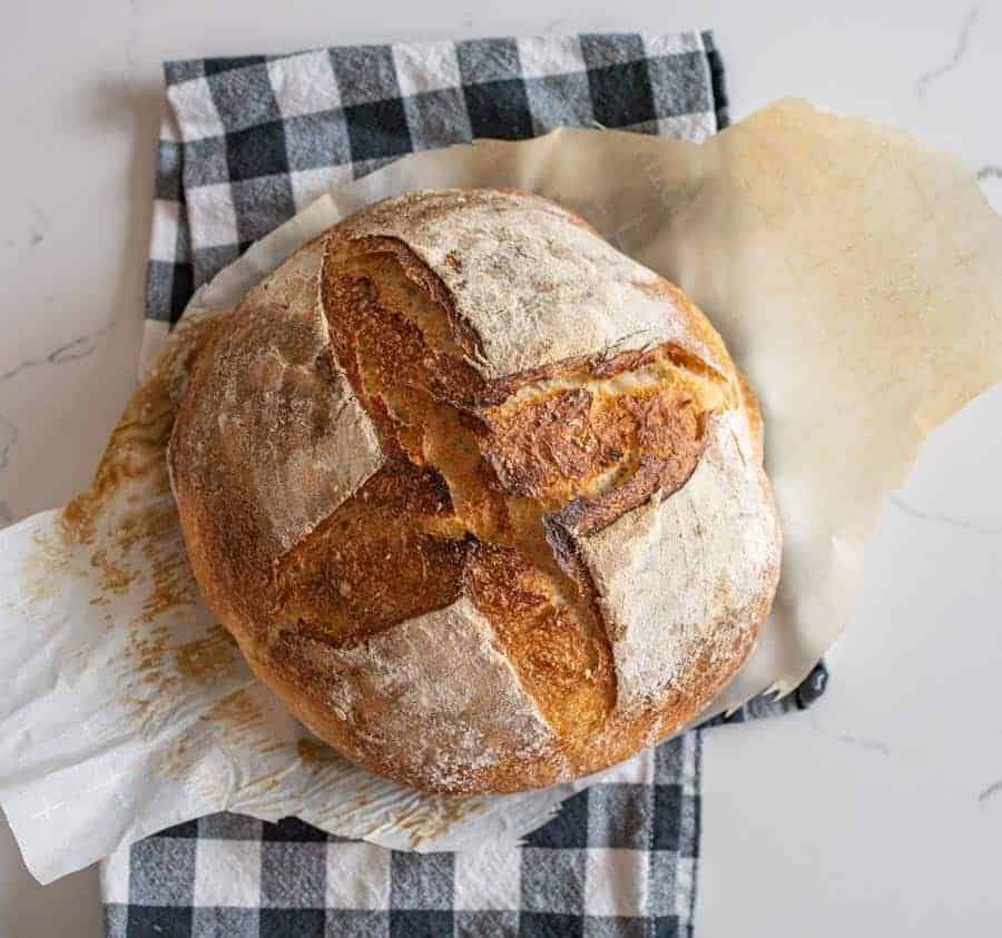 loaf of sourdough bread on parchment and black and white towel.