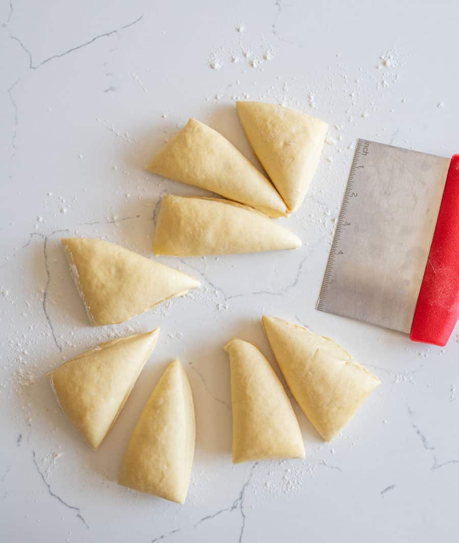 Sourdough hamburger bun dough cut into eight equal portions on a lightly floured white counter. 