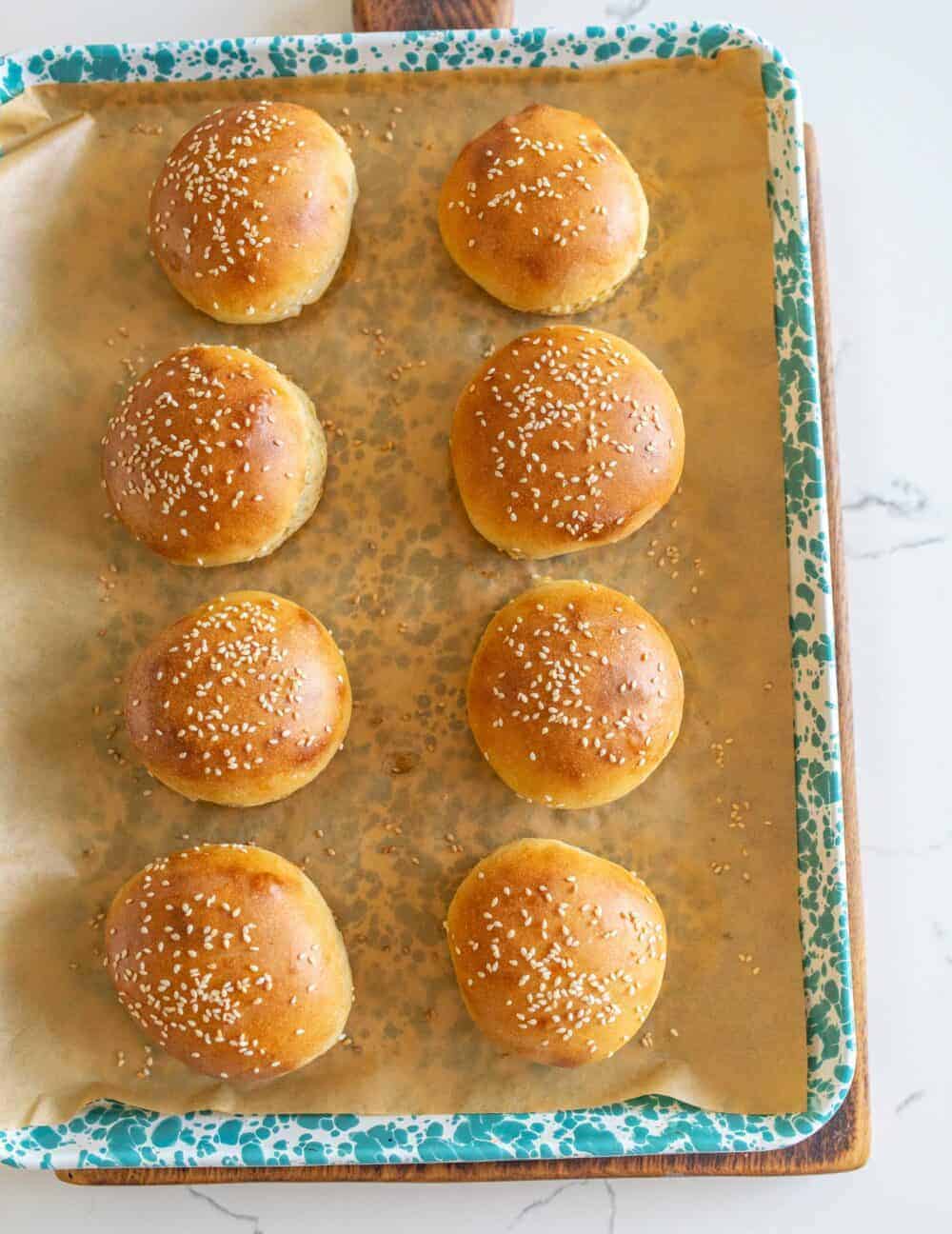 Sourdough burger buns on parchment paper on a blue and white enamelware pan after baking.