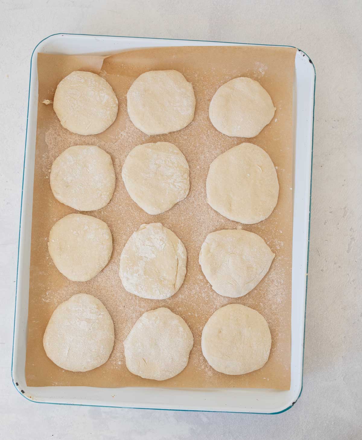 unbaked sourdough english muffins on white sheet pan.