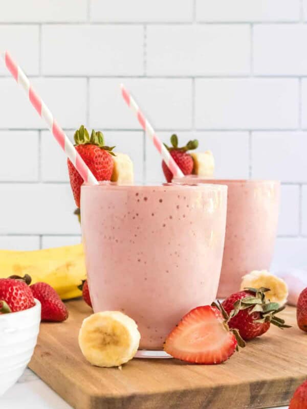 strawberry banana smoothies in cups with pink striped paper straws and fresh fruit all around