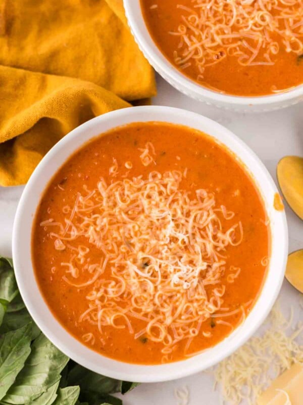 two white bowls with tomato basil soup and cheese on top.