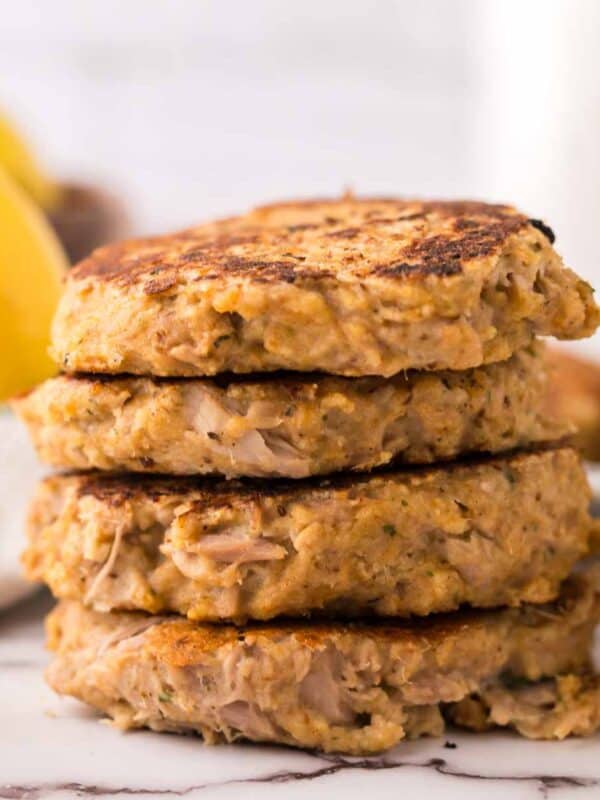 four tuna patties in a stack with fresh lemons to the side.