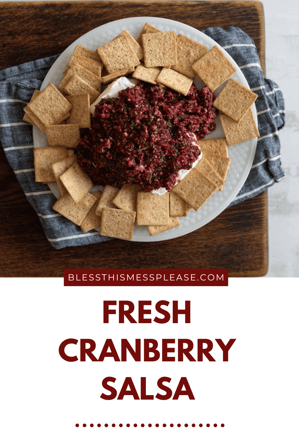 A plate with fresh cranberry salsa surrounded by square crackers, placed on a wooden board with a blue napkin. Text reads: BLESSTHISMESSPLEASE.COM Fresh Cranberry Salsa.